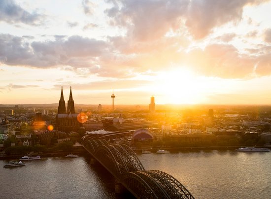 Panoramablick auf die Stadt Köln mit dem Kölner Dom bei Sonnenuntergang. Im Vordergrund die Hohenzollernbrücke, die über den Rhein führt.