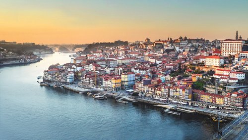 Blick auf die Altstadt von Porto am Douro-Fluss bei Sonnenuntergang mit bunten Häusern und Brücke im Vordergrund.