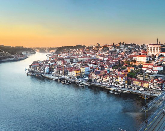 Blick auf die Altstadt von Porto am Douro-Fluss bei Sonnenuntergang mit bunten Häusern und Brücke im Vordergrund.