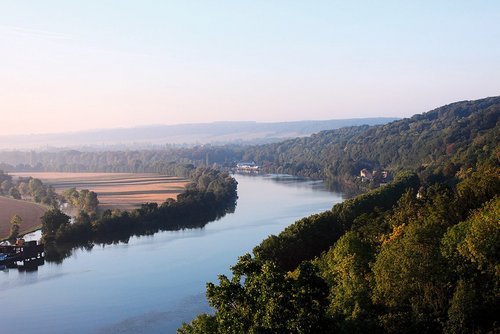 Fluss Seine fließt durch bewaldete Hügel und Felder bei klarem Himmel in der Normandie.