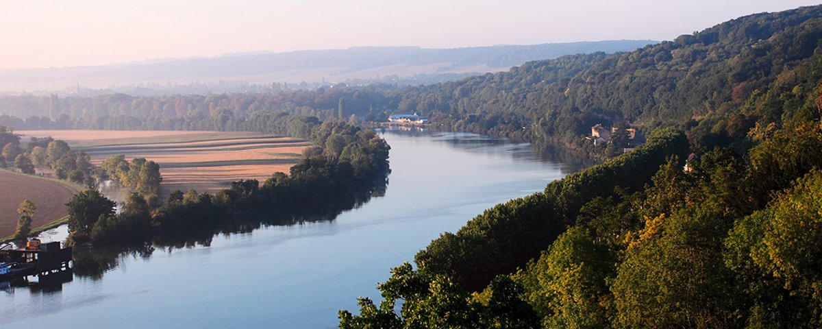 Fluss Seine fließt durch bewaldete Hügel und Felder bei klarem Himmel in der Normandie. 