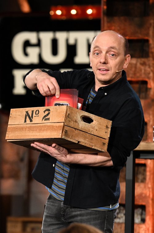 Wigald Boning und Bernhard Hoëcker während der Aufzeichnung für Ihre Sendung "Gute Frage". Bernhard Hoëcker hält eine Holzkiste und Karteikarten in der Hand. Wigald Boning trägt ein rotes Hemd und hat die Hände an der Hüfte.