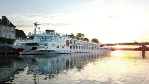 Flusskreuzfahrtschiff A-ROSA VIVA am Ufer bei Sonnenuntergang mit Brücke im Hintergrund.