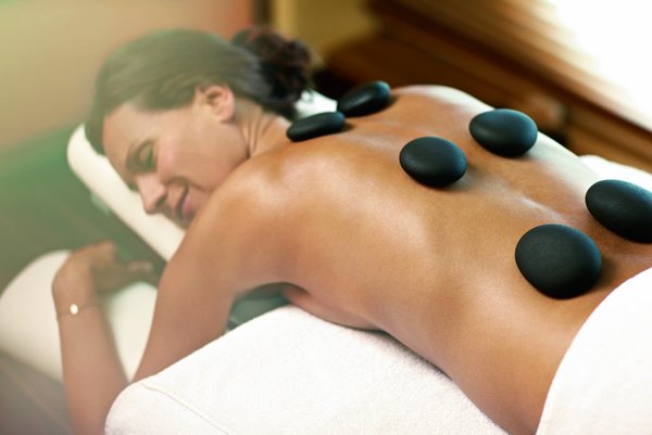 Eine Frau liegt entspannt auf einer Massageliege im SPA-ROSA, während heiße Steine auf ihrem Rücken platziert werden, um Entspannung zu fördern.