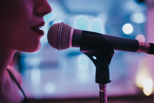Nahaufnahme einer Sängerin, die in ein Mikrofon singt, mit unscharfem Hintergrund und blauer Beleuchtung.