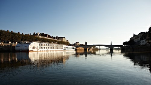 Die A-ROSA STELLA liegt am Ufer in einer Stadt an der Rhône bei Sonnenaufgang, im Hintergrund eine Brücke und Gebäude. 