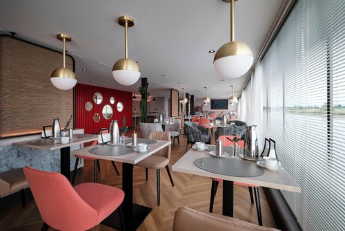 Stilvoll eingedeckter Restaurantbereich der A-ROSA SENA mit bodentiefen Fenstern und Blick auf einen ruhigen Fluss.