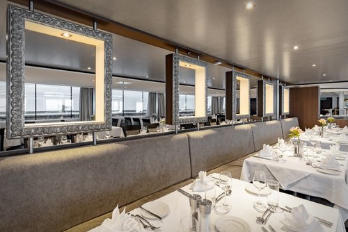 Stilvoll eingedeckter Restaurantbereich der A-ROSA ALEA mit Fenstern, Blumendeko und gedämpfter Beleuchtung.