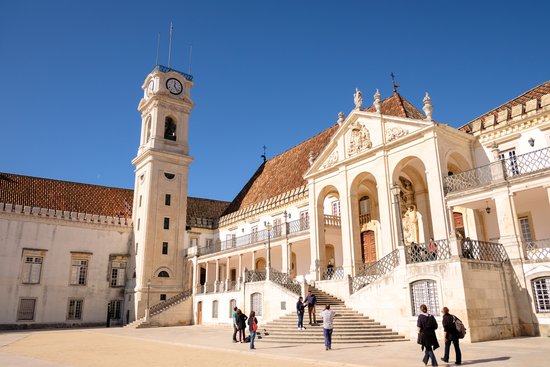 Historisches Universitätsgebäude in Coimbra mit Uhrturm, Arkaden und Treppen, Menschen im Vordergrund bei sonnigem Wetter