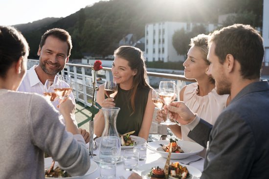Yvonne Catterfeld und vier weitere Personen sitzen beim Abendessen und Wein auf dem Sonnendeck, Sonnenlicht im Hintergrund.