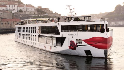 Flusskreuzfahrtschiff A-ROSA ALVA auf dem Douro vor einer Stadt mit historischen Gebäuden und roten Dächern.