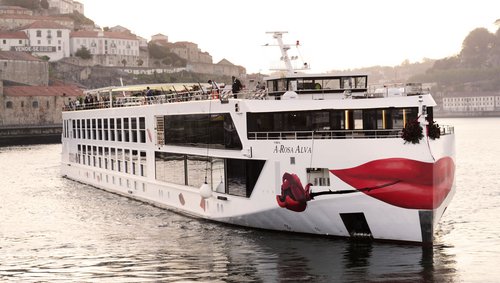 Flusskreuzfahrtschiff A-ROSA ALVA auf dem Douro vor einer Stadt mit historischen Gebäuden und roten Dächern.