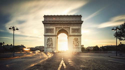 Sonnenuntergang hinter dem Arc de Triomphe in Paris mit Lichtspuren auf der Straße. 