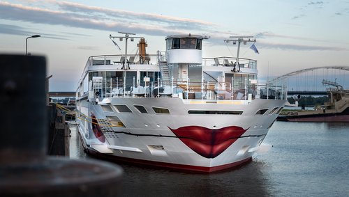 Die A-ROSA SENA mit Kussmund und Rose um Bug liegt am Abend am Anleger in einem Hafen, der Himmel ist leicht bewölkt.