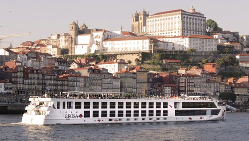Flusskreuzfahrtschiff A-ROSA ALVA auf dem Douro vor einer Stadt mit historischen Gebäuden und roten Dächern.