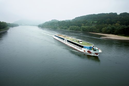 Das Flusskreuzfahrtschiff A-ROSA MIA auf der Donau durch die Wachau, umgeben vom ruhigen Fluss und dem dicht bewachsenen Ufer mit nebeliger Hügellandschaft.